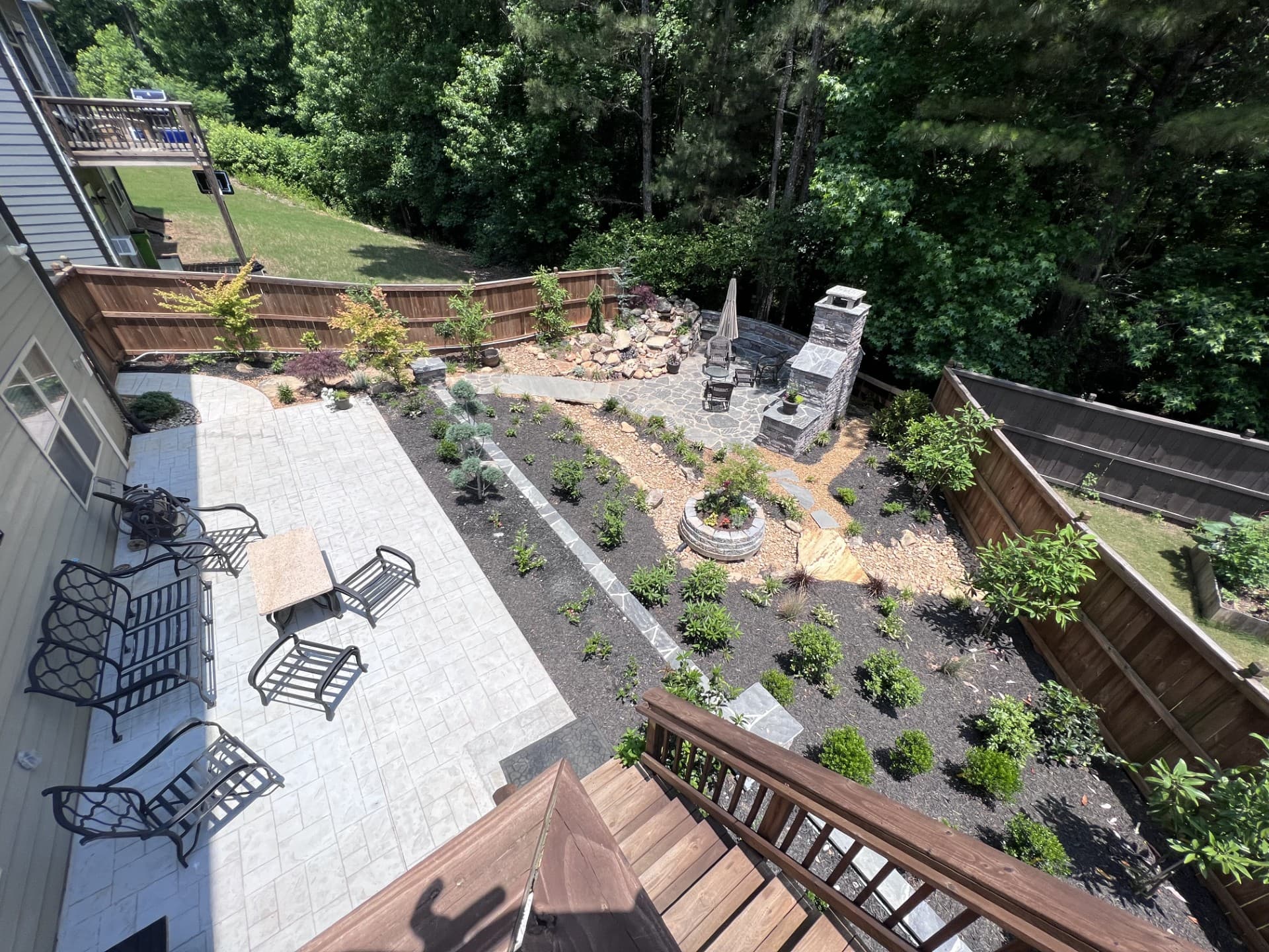 Landscaped backyard featuring a stone patio, seating, garden beds, and an outdoor stone fireplace.