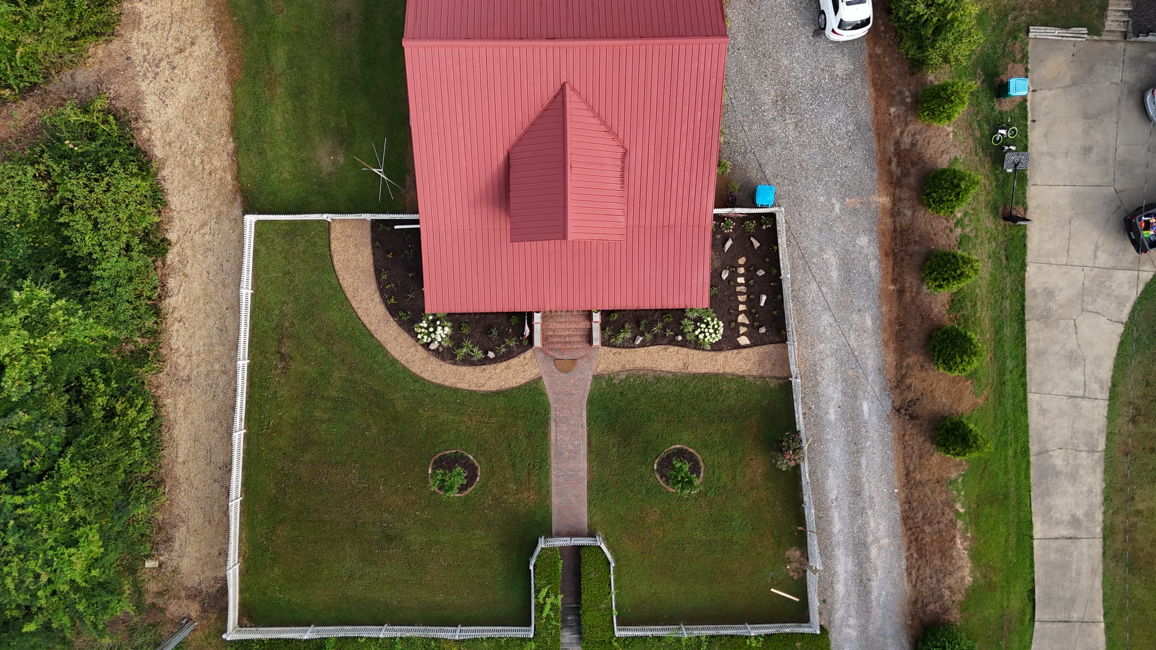 Aerial view of a house with a red metal roof and white picket fence.