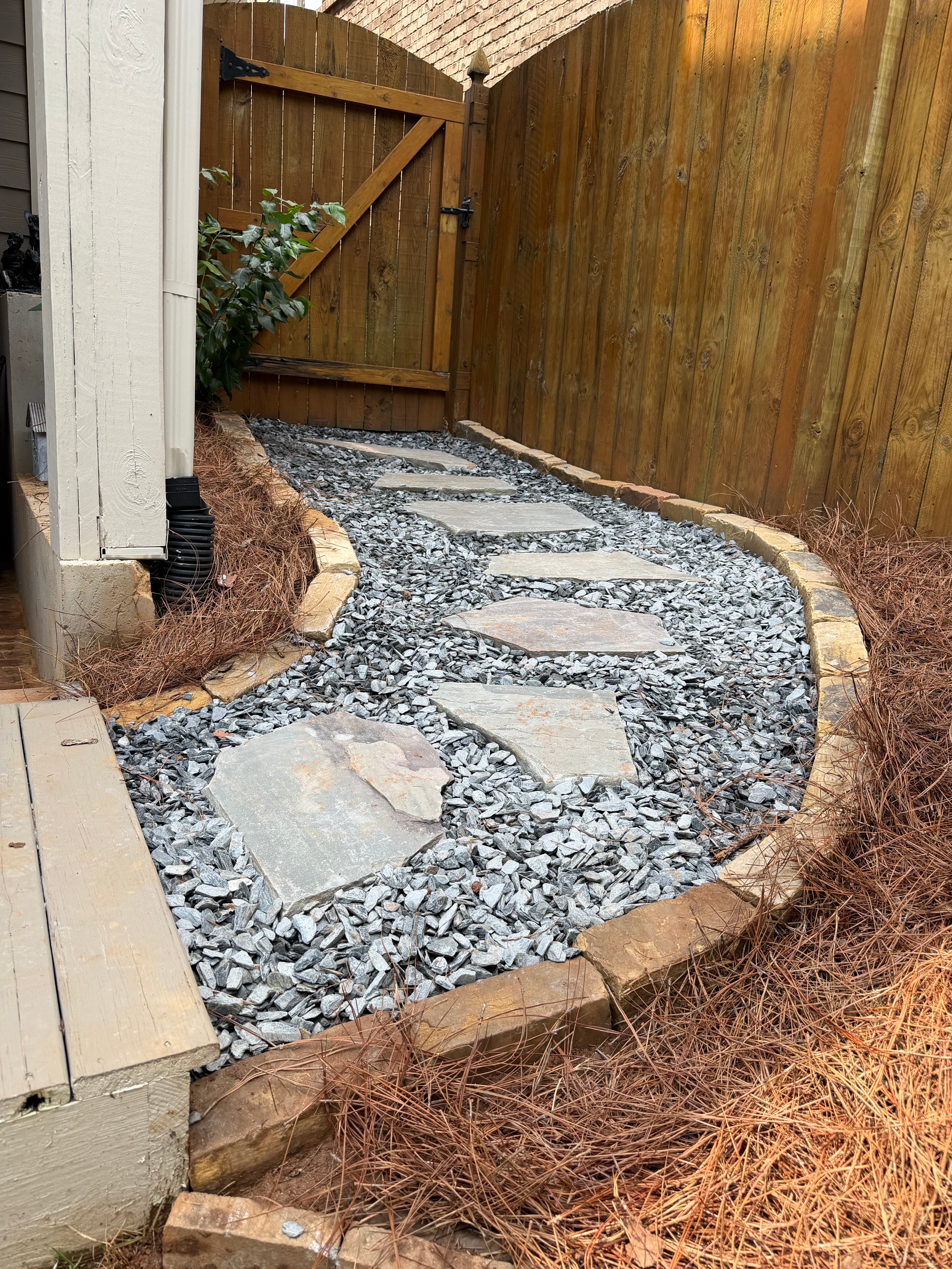 Curved gravel garden path with flagstone stepping stones leading toward a wooden gate.