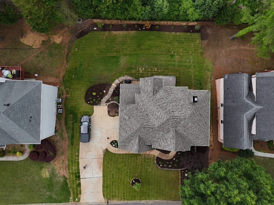 Aerial view of a suburban home with a grey roof, driveway, and manicured green lawn.