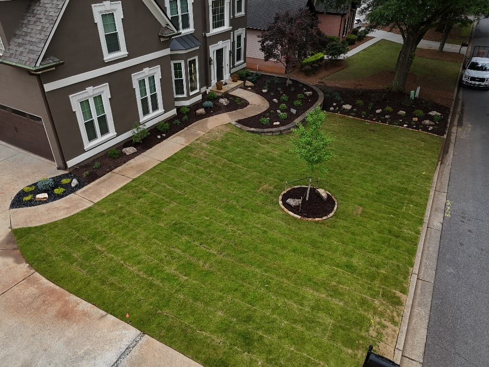 Aerial view of a brown house with new sod lawn and a curved concrete walkway.