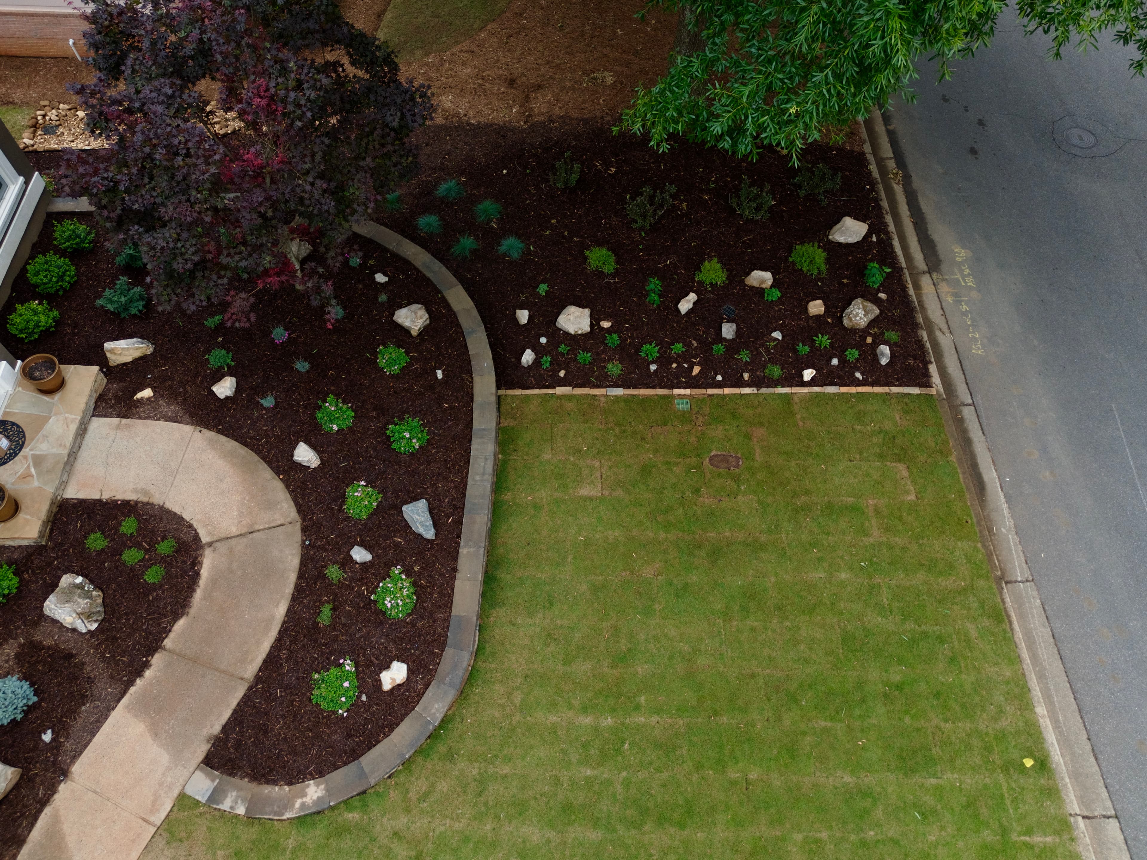 Aerial view of a landscaped yard with a curved walkway, dark mulch, and green lawn.